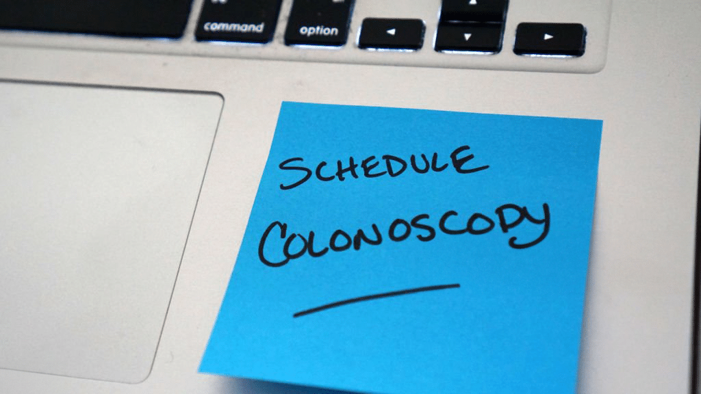 A sticky note on laptop reminding to schedule colonoscopy. 