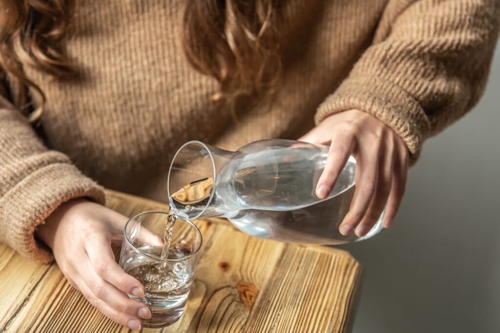 Woman pouring water into glass, drinking water to stay hydrated for a healthy gut.